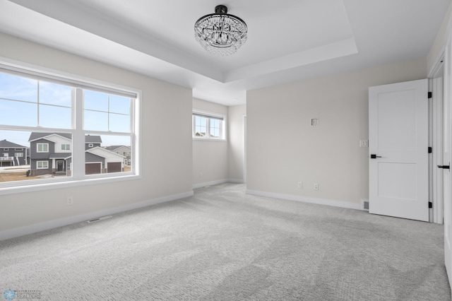 carpeted spare room featuring a chandelier, a raised ceiling, visible vents, and baseboards