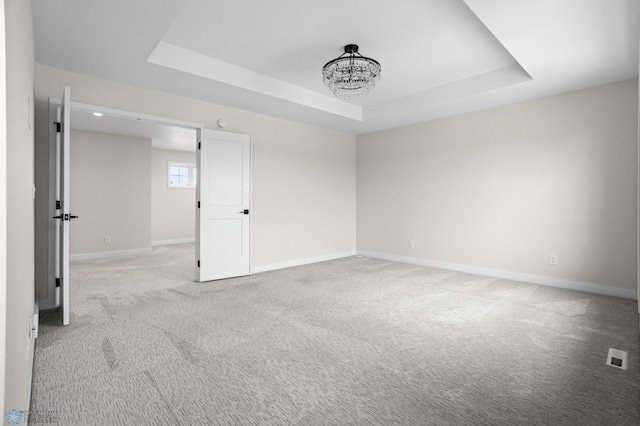 unfurnished room featuring a chandelier, a raised ceiling, light colored carpet, and baseboards