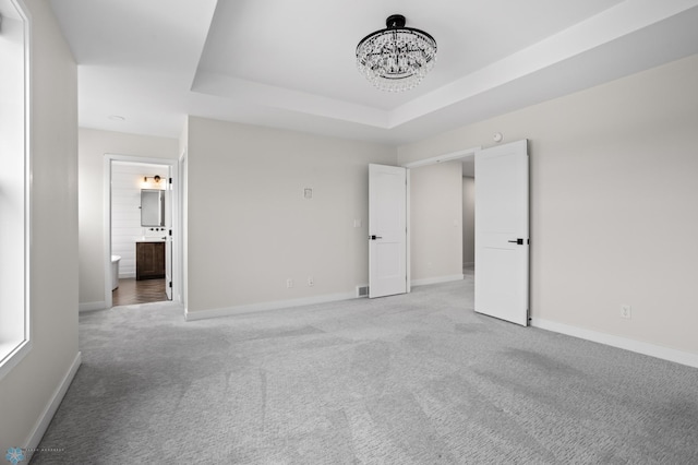 unfurnished bedroom featuring a tray ceiling, light colored carpet, a notable chandelier, and baseboards