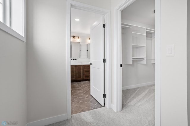 hall featuring carpet floors, a sink, and baseboards