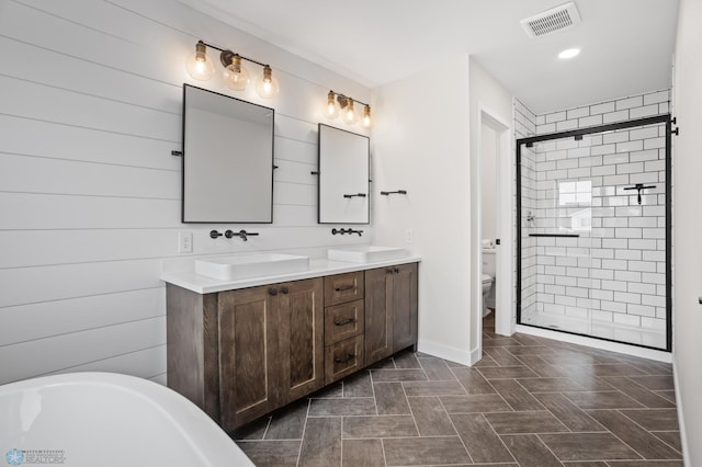 bathroom featuring toilet, a stall shower, a sink, and visible vents