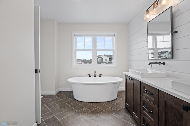 bathroom featuring a freestanding bath, double vanity, a sink, and baseboards