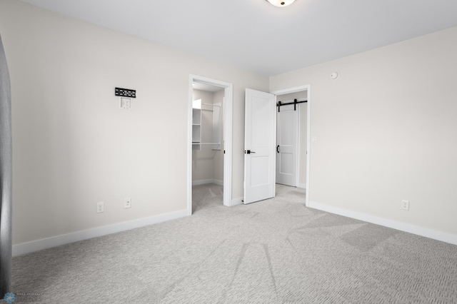 unfurnished bedroom with a barn door, baseboards, a spacious closet, carpet flooring, and a closet