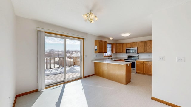 kitchen with light countertops, appliances with stainless steel finishes, a peninsula, brown cabinetry, and a sink