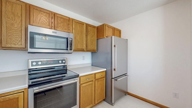 kitchen featuring light countertops, baseboards, brown cabinets, and appliances with stainless steel finishes