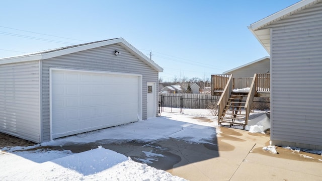 snow covered garage featuring a garage and fence