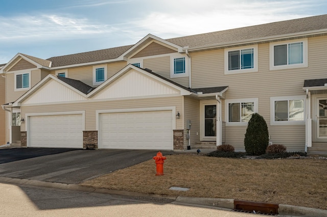 townhome / multi-family property with a shingled roof, aphalt driveway, entry steps, stone siding, and an attached garage