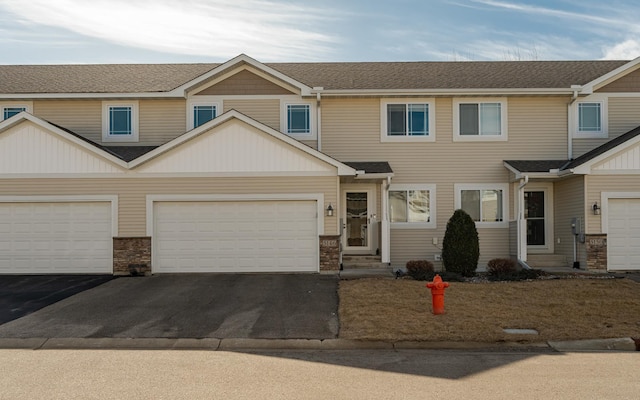 townhome / multi-family property with a garage, stone siding, driveway, and a shingled roof
