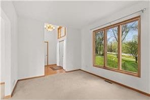 carpeted empty room with plenty of natural light, a chandelier, and baseboards