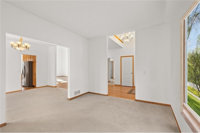 spare room featuring baseboards, visible vents, a notable chandelier, and light colored carpet