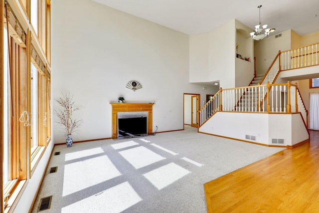 carpeted living area featuring a fireplace with flush hearth, a towering ceiling, visible vents, stairs, and an inviting chandelier