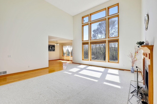 carpeted living room with a fireplace, wood finished floors, a towering ceiling, and baseboards