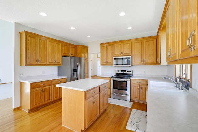 kitchen featuring light wood finished floors, a center island, stainless steel appliances, light countertops, and a sink