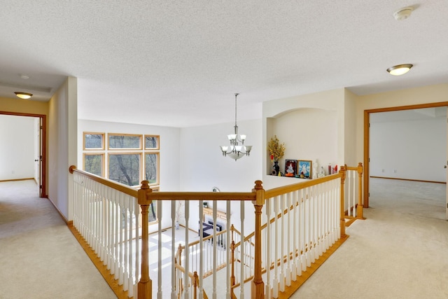 hallway with a textured ceiling, light carpet, an upstairs landing, baseboards, and an inviting chandelier