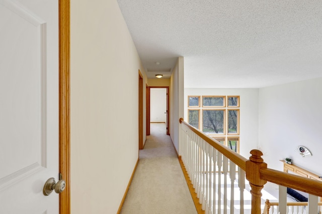 hall with baseboards, light carpet, a textured ceiling, and an upstairs landing