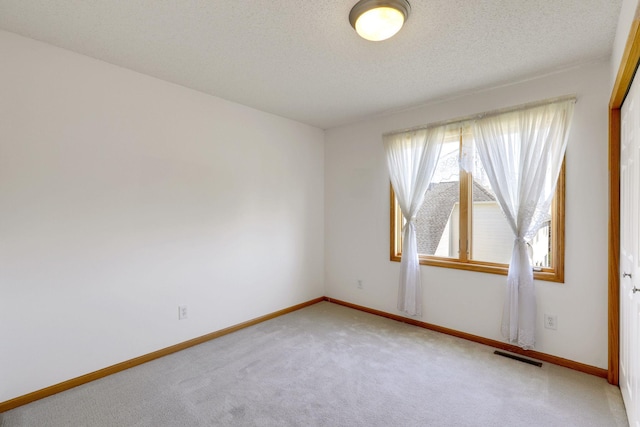 spare room with a textured ceiling, carpet, visible vents, and baseboards