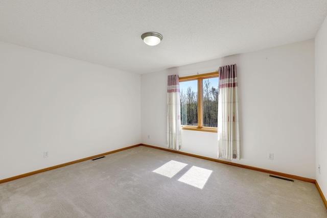 empty room featuring carpet, a textured ceiling, visible vents, and baseboards