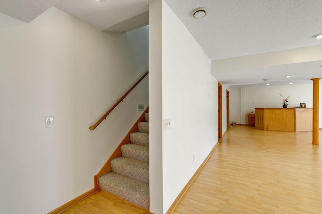 staircase featuring a textured ceiling, wood finished floors, and baseboards