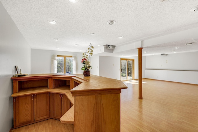 kitchen featuring a textured ceiling, baseboards, open floor plan, light wood finished floors, and ornate columns