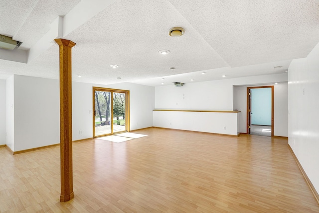 unfurnished living room with light wood-type flooring, ornate columns, baseboards, and a textured ceiling