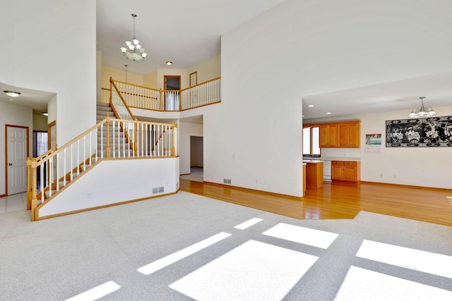 unfurnished living room with a notable chandelier, visible vents, stairs, a towering ceiling, and light colored carpet
