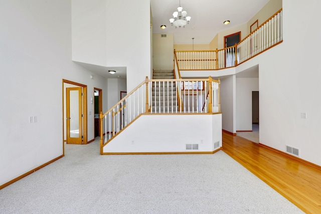 unfurnished living room with stairs, a towering ceiling, baseboards, visible vents, and a notable chandelier