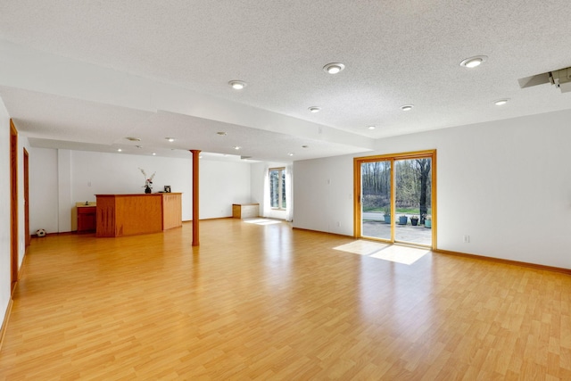unfurnished living room with light wood-style flooring, a textured ceiling, baseboards, and ornate columns