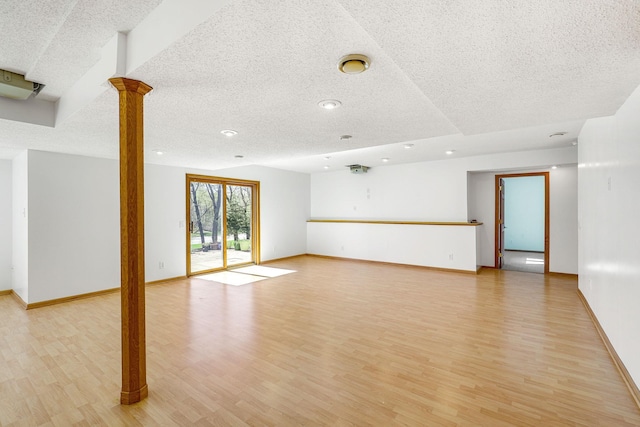 unfurnished living room featuring decorative columns, a textured ceiling, recessed lighting, light wood-style flooring, and baseboards