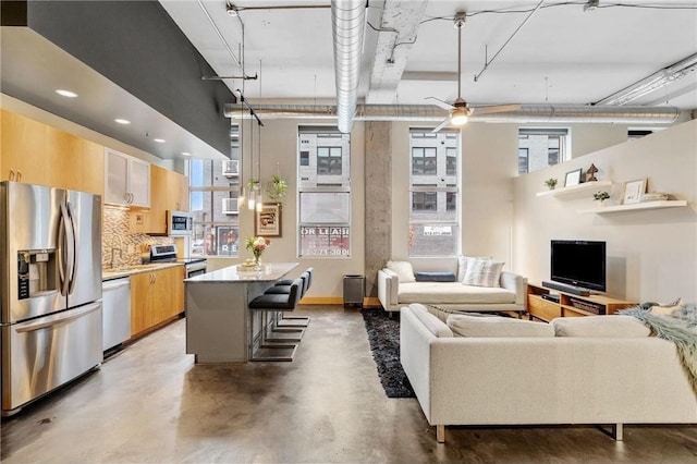 kitchen with stainless steel appliances, a breakfast bar, open floor plan, finished concrete flooring, and tasteful backsplash