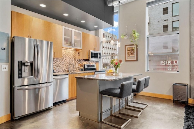 kitchen featuring light stone counters, decorative backsplash, appliances with stainless steel finishes, a kitchen island, and concrete floors