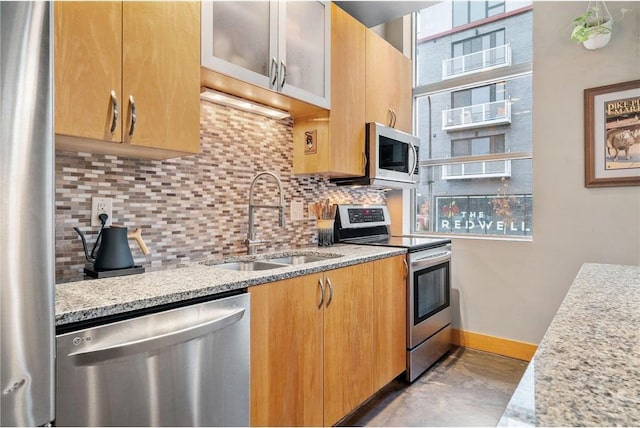 kitchen featuring decorative backsplash, appliances with stainless steel finishes, a sink, light stone countertops, and baseboards