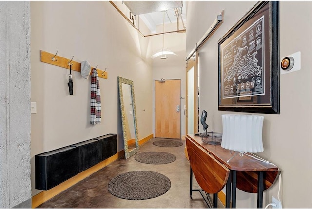 corridor featuring finished concrete flooring, a towering ceiling, and baseboards