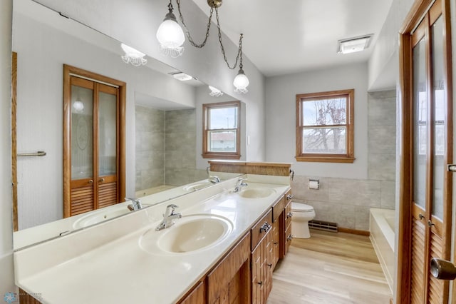 3129 7th St N, Fargo, ND 58102 - bathroom with toilet, double vanity, wood finished floors, a bath, and tile walls