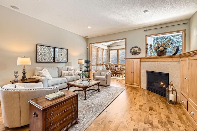 living room with a textured ceiling, a tiled fireplace, and light wood-style flooring