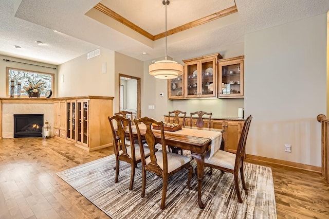 dining area with a textured ceiling, a tray ceiling, light wood-style flooring, and visible vents