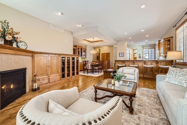 living area with recessed lighting, visible vents, a tiled fireplace, a textured ceiling, and light wood-type flooring