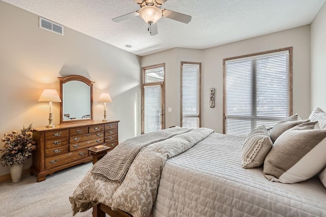 bedroom featuring a ceiling fan, light colored carpet, visible vents, and a textured ceiling