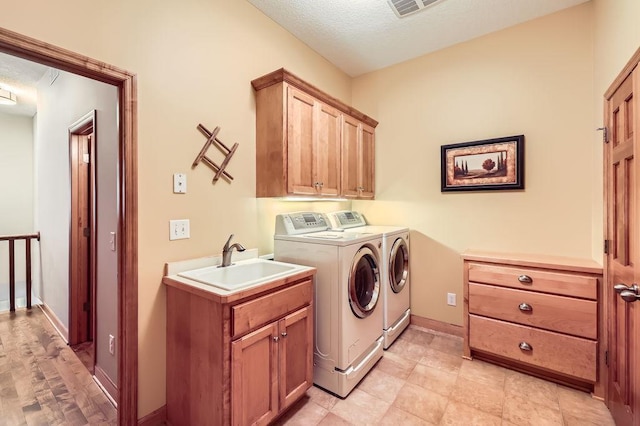 washroom with a textured ceiling, a sink, baseboards, washer and dryer, and cabinet space