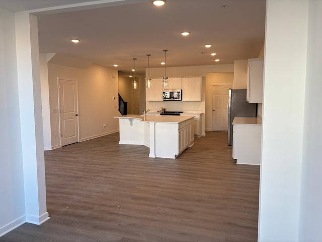 kitchen featuring recessed lighting, stainless steel appliances, white cabinetry, baseboards, and a center island with sink