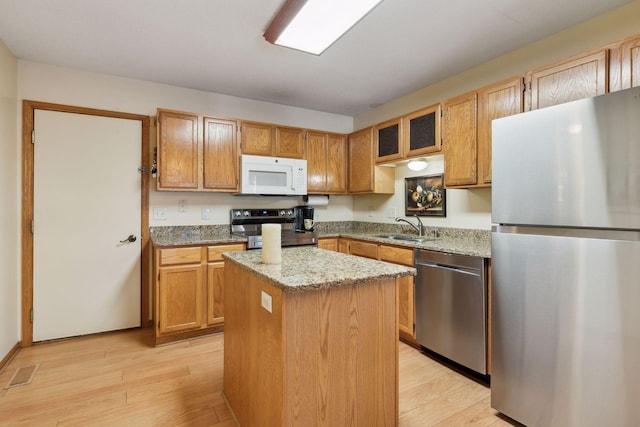 kitchen with appliances with stainless steel finishes, a center island, light wood-style floors, and a sink