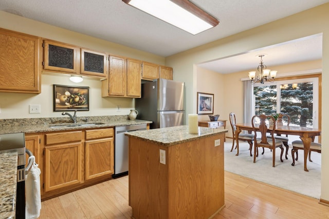 kitchen with stainless steel appliances, a sink, a center island, light wood-style floors, and light stone countertops