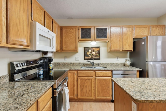 kitchen with light stone counters, stainless steel appliances, a sink, a textured ceiling, and light wood-type flooring