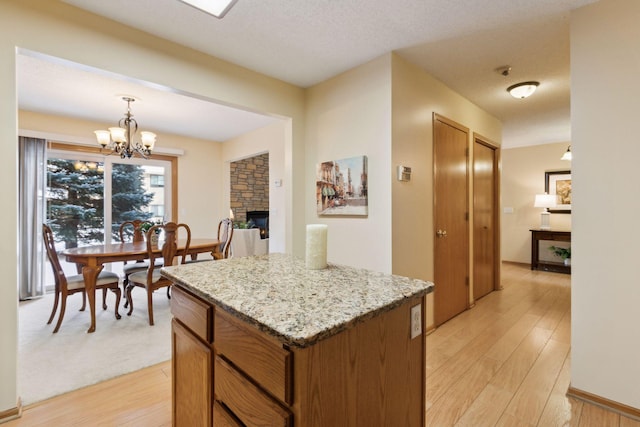 kitchen featuring hanging light fixtures, a stone fireplace, light wood-style flooring, and brown cabinets