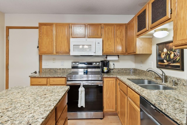 kitchen with light wood-style flooring, appliances with stainless steel finishes, light stone counters, and a sink