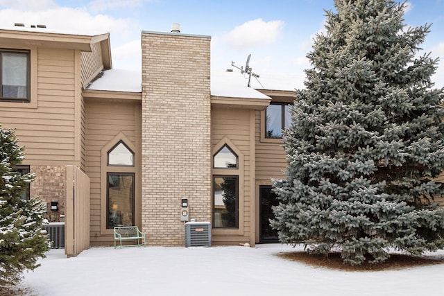 view of front facade with brick siding, a chimney, and central AC unit