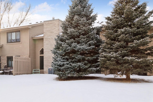 exterior space with brick siding, a chimney, cooling unit, and fence