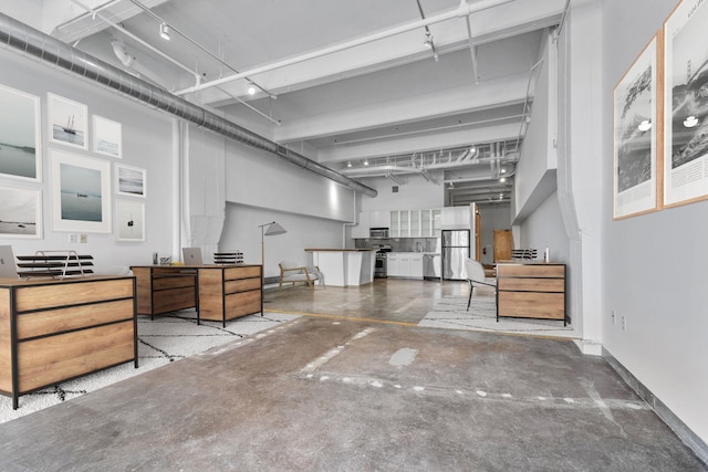 miscellaneous room featuring concrete flooring, a towering ceiling, and baseboards