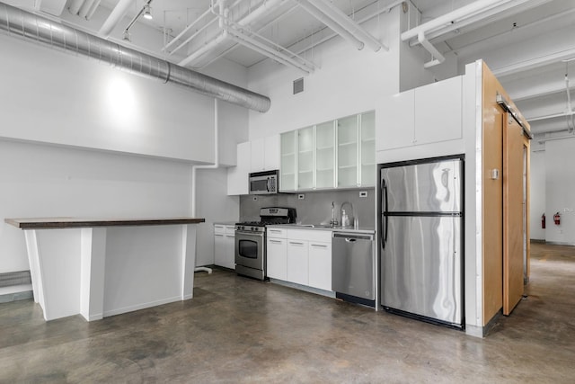 kitchen featuring finished concrete flooring, stainless steel appliances, visible vents, a high ceiling, and white cabinetry