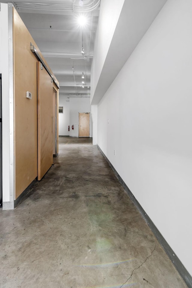 hall featuring concrete floors, baseboards, and a barn door