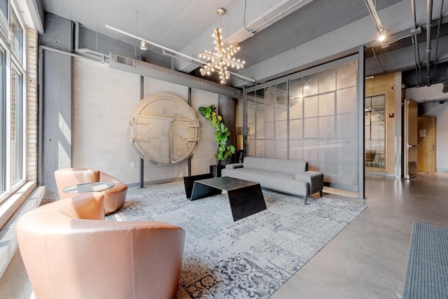 living room featuring finished concrete floors, concrete block wall, visible vents, rail lighting, and an inviting chandelier